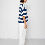 Person wearing a blue and white striped T-shirt with white pants on a plain background