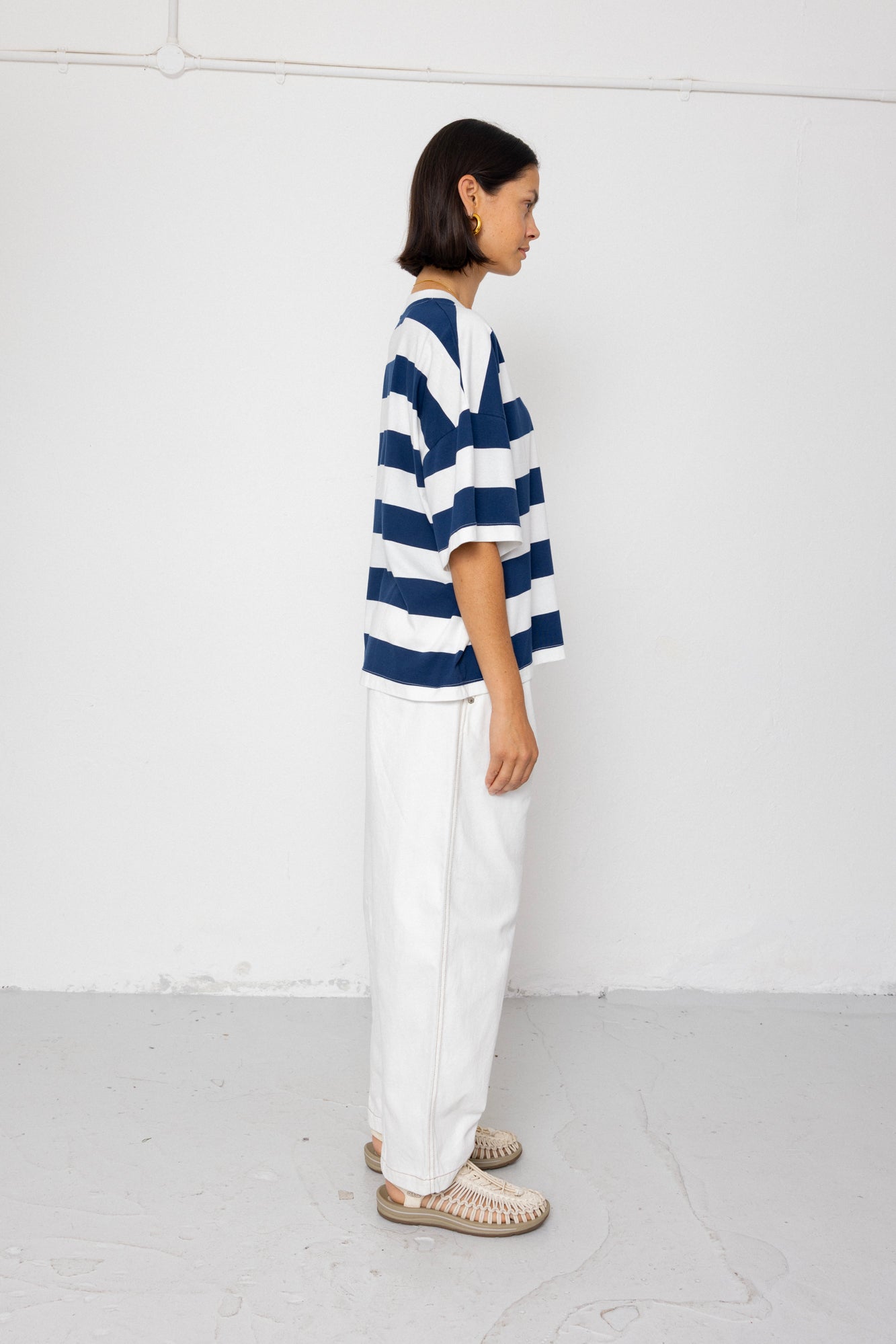 Person wearing a blue and white striped T-shirt with white pants on a plain background