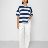 Person wearing a blue and white striped T-shirt with white pants on a plain background