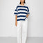 Person wearing a blue and white striped T-shirt with white pants on a plain background