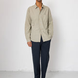 Man wearing a beige shirt and dark pants against a white background