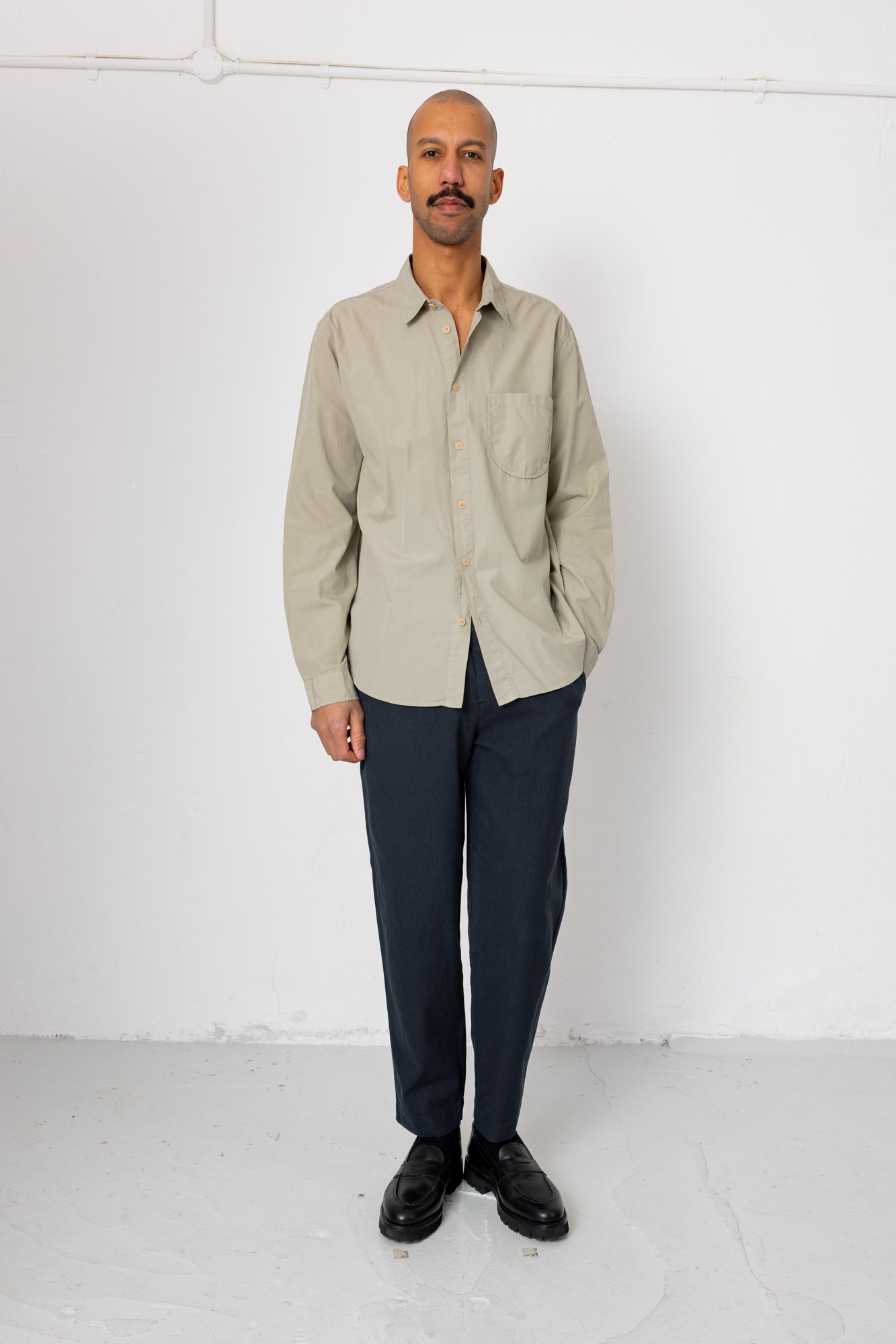 Man wearing a beige shirt and dark pants against a white background