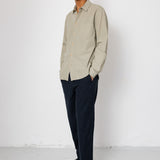 Man wearing a beige shirt and dark pants against a white background