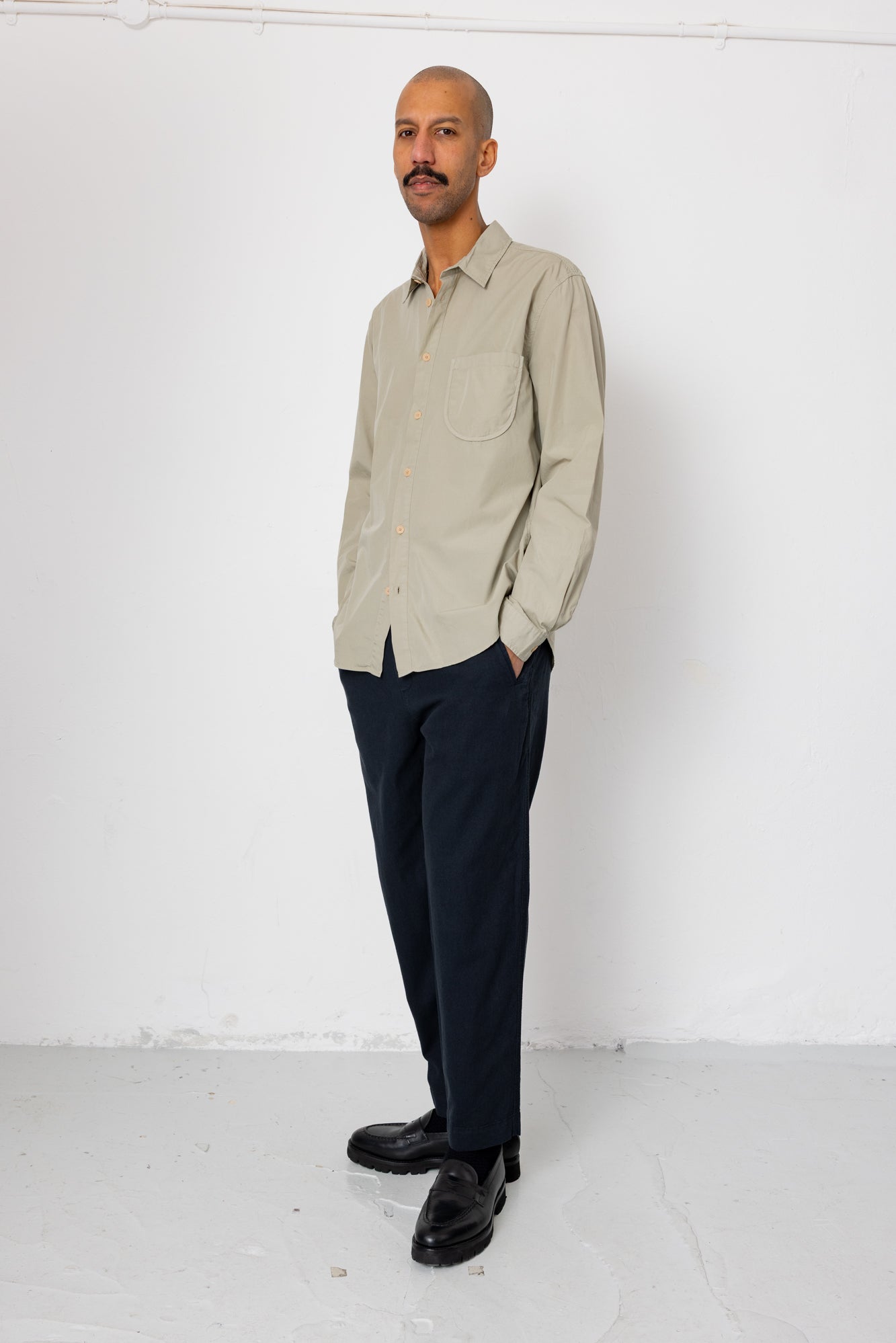 Man wearing a beige shirt and dark pants against a white background