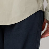 Close-up of a person wearing a beige shirt and dark pants on a light gray background