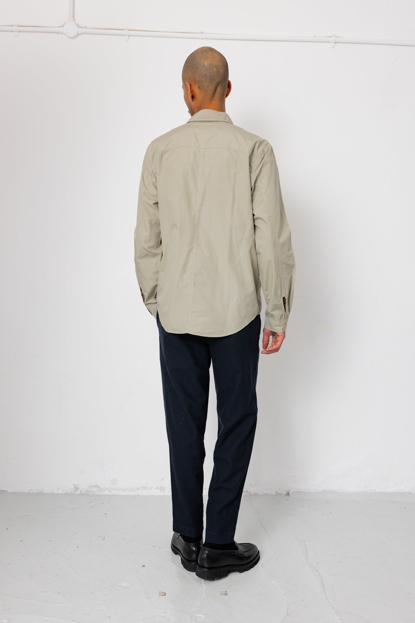 Man wearing a beige shirt and dark pants against a white background