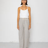 Woman wearing white tank top with grey and white striped pants against a white background