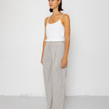 Woman wearing white tank top with grey and white striped pants against a white background