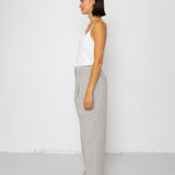 Woman wearing white tank top with grey and white striped pants against a white background