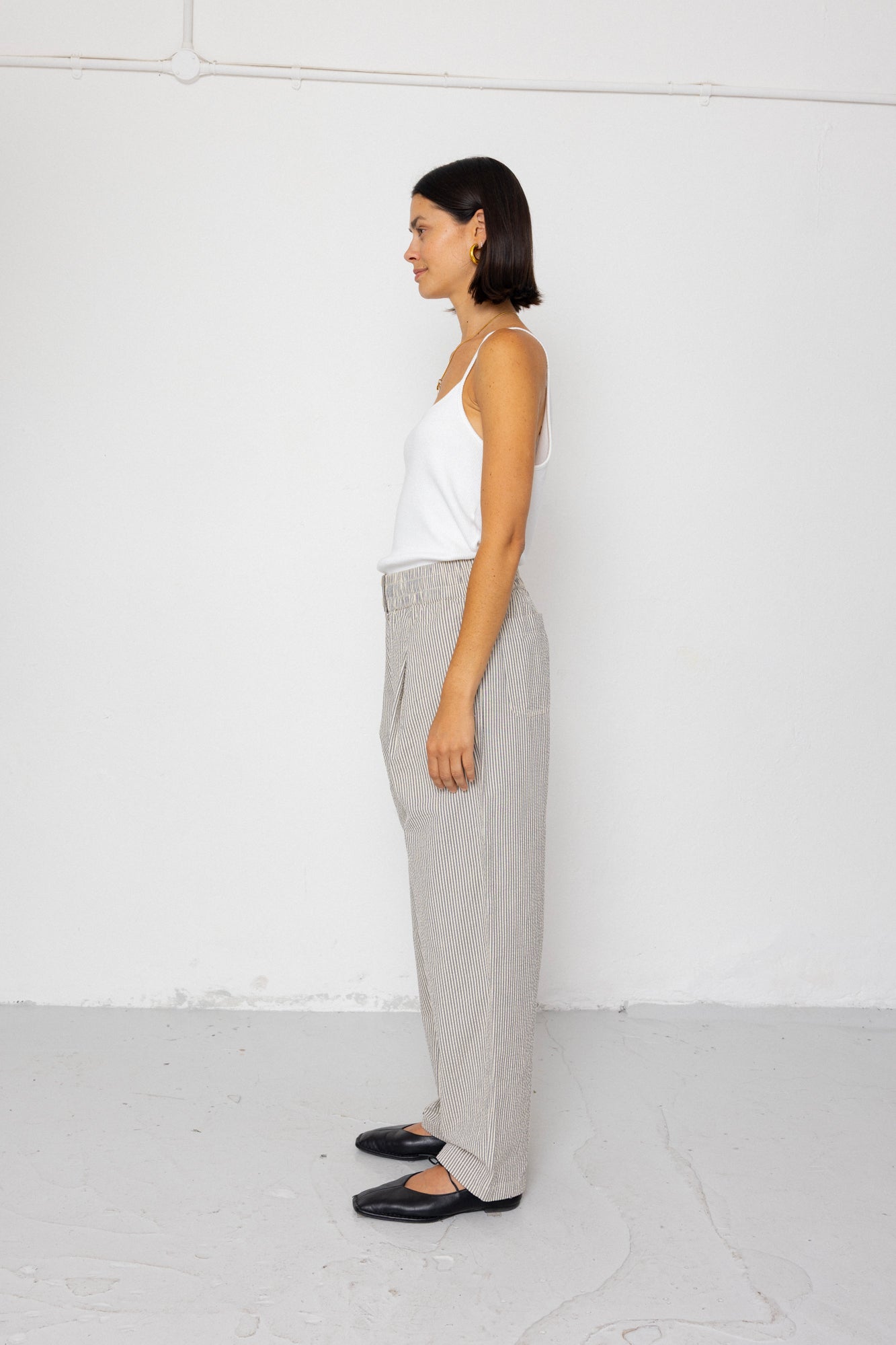 Woman wearing white tank top with grey and white striped pants against a white background