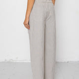 Woman wearing white tank top with grey and white striped pants against a white background
