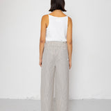 Woman wearing white tank top with grey and white striped pants against a white background