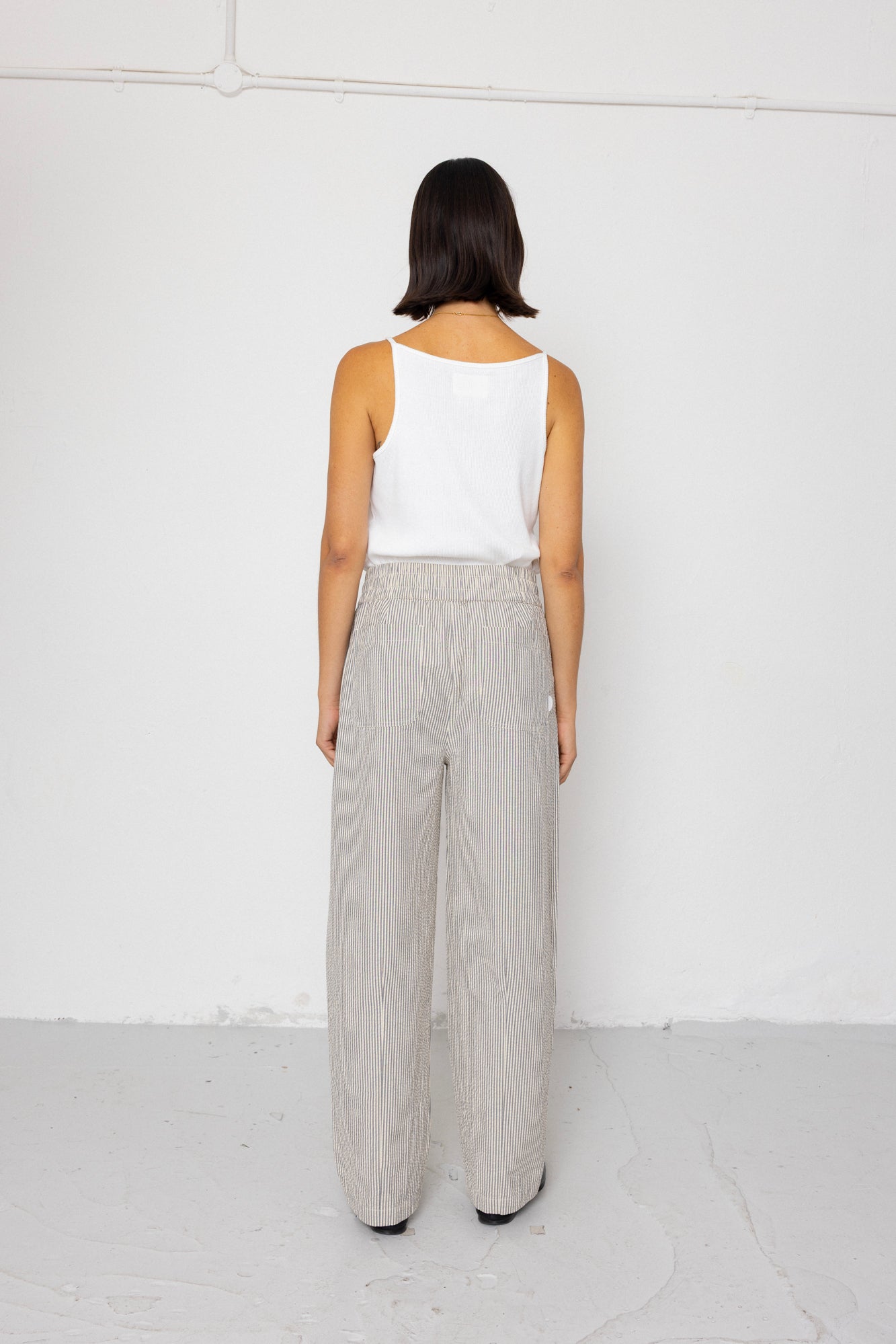 Woman wearing white tank top with grey and white striped pants against a white background