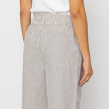 Woman wearing white tank top with grey and white striped pants against a white background