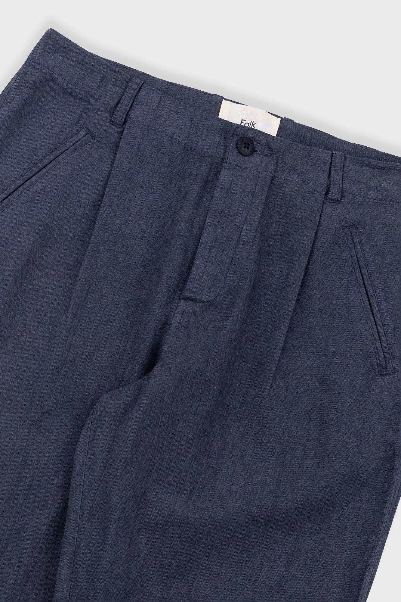 Navy blue pleated pants with a brand label on a white background