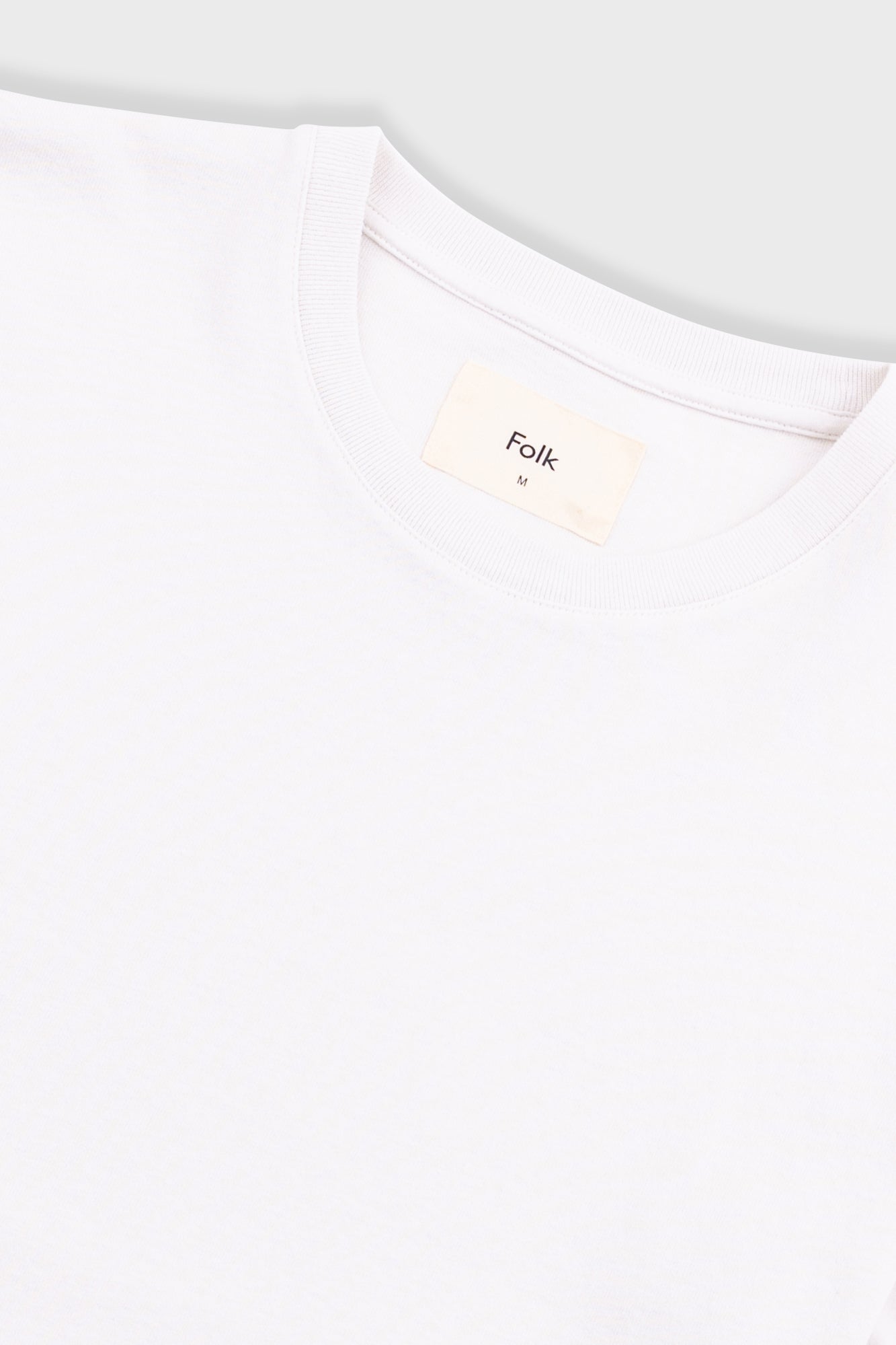 Close-up of a white t-shirt with 'Folk' brand label on a light gray background