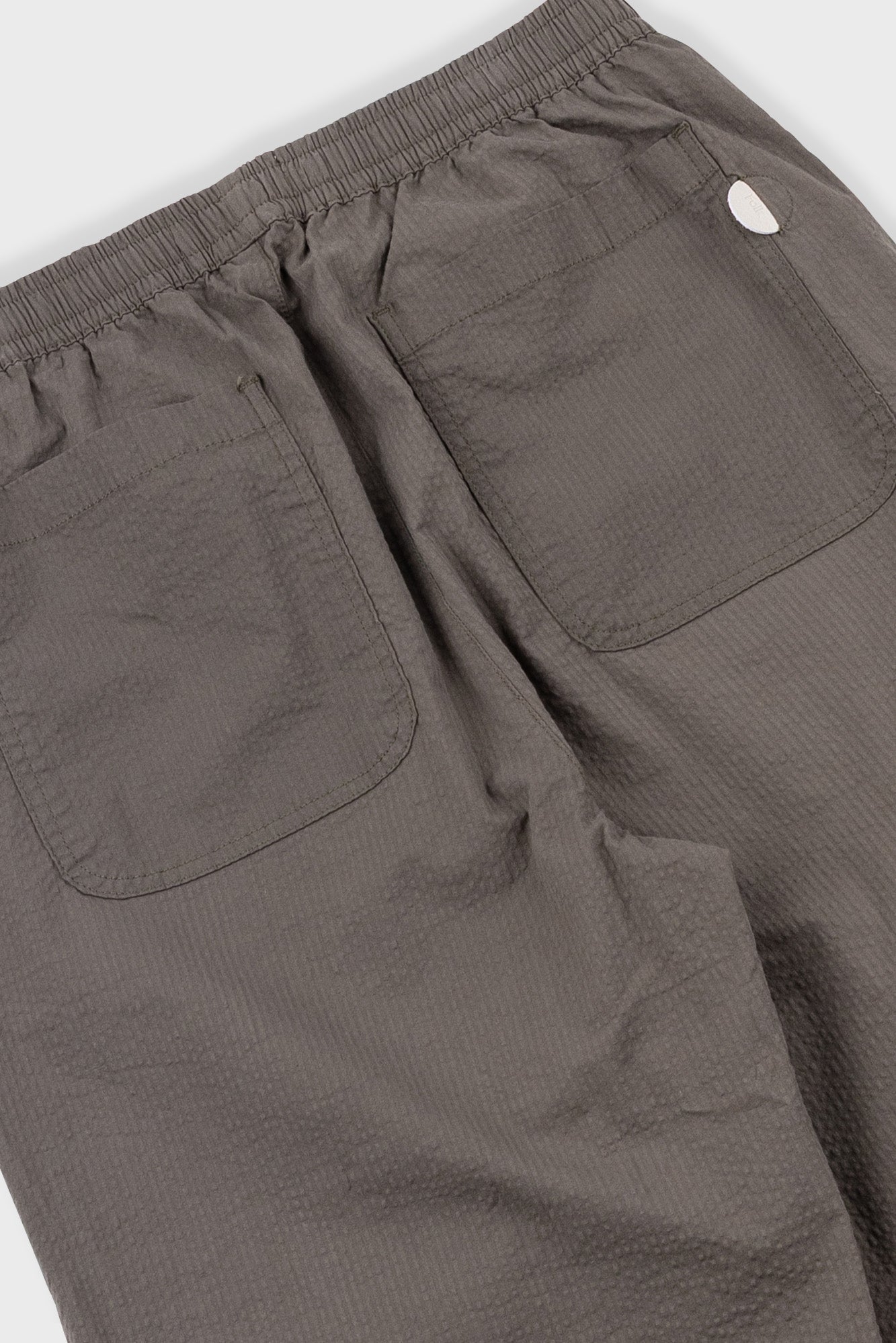 Close-up of brown pants with a visible brand logo on a white background