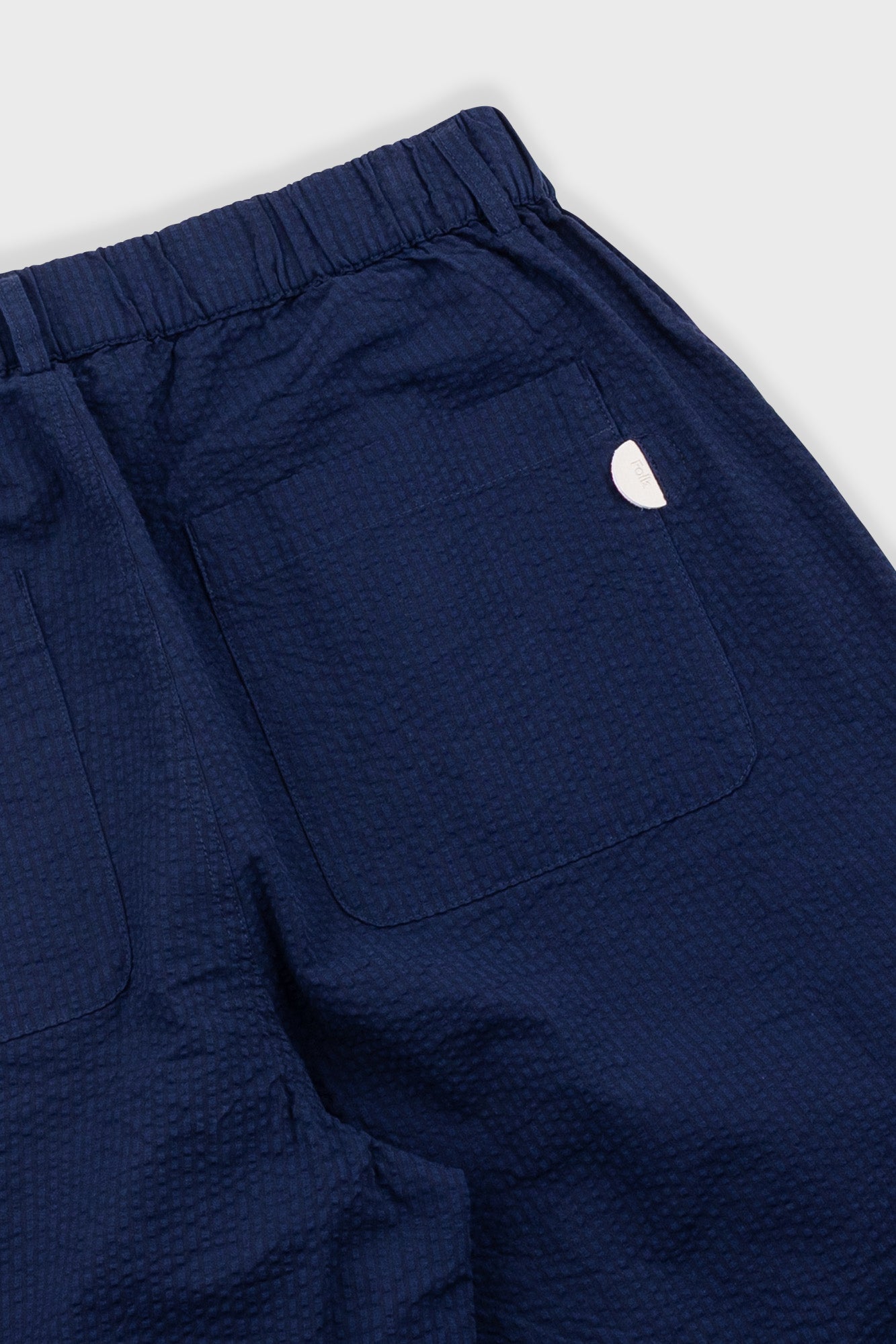 Close-up of navy blue pants with a small white logo on a light gray background