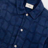 Close-up of a blue textured shirt with buttons and a visible brand label on a white background