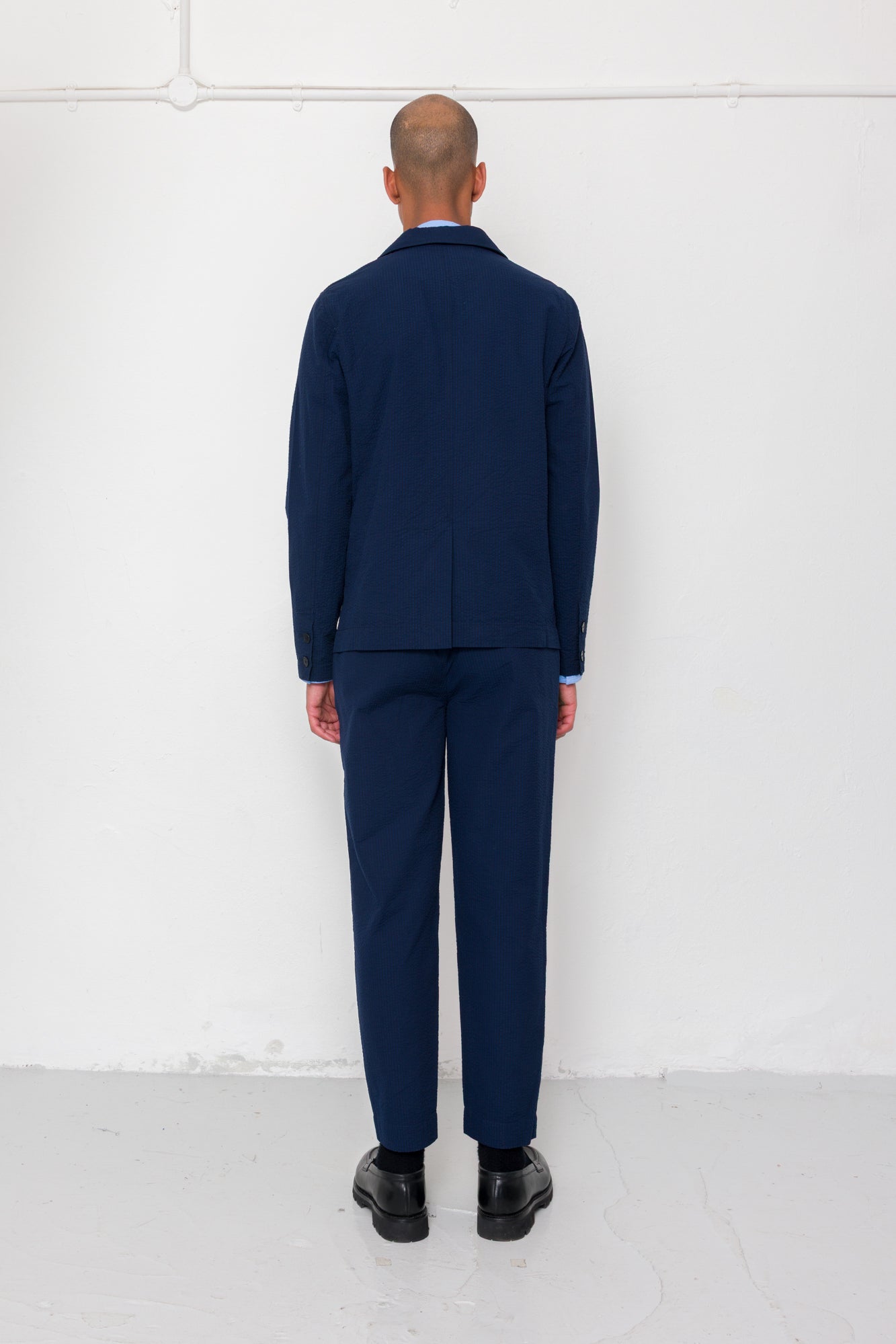 Person wearing a navy blue suit standing against a white wall