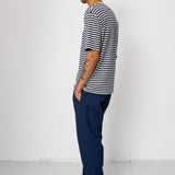 Man wearing a striped shirt and blue pants standing against a white wall.