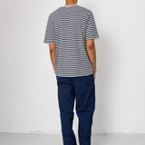 Man wearing a striped shirt and blue pants standing against a white wall.