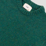 Close-up of a green textured sweater with a brand tag on a gray background