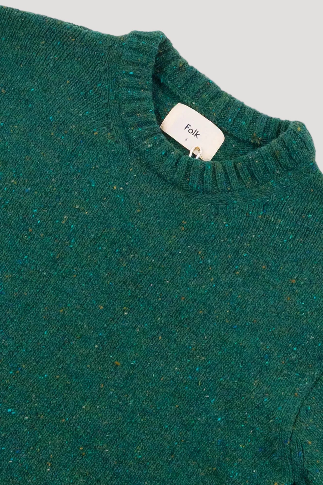 Close-up of a green textured sweater with a brand tag on a gray background