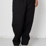Person wearing black pants and gray sneakers against a white wall.