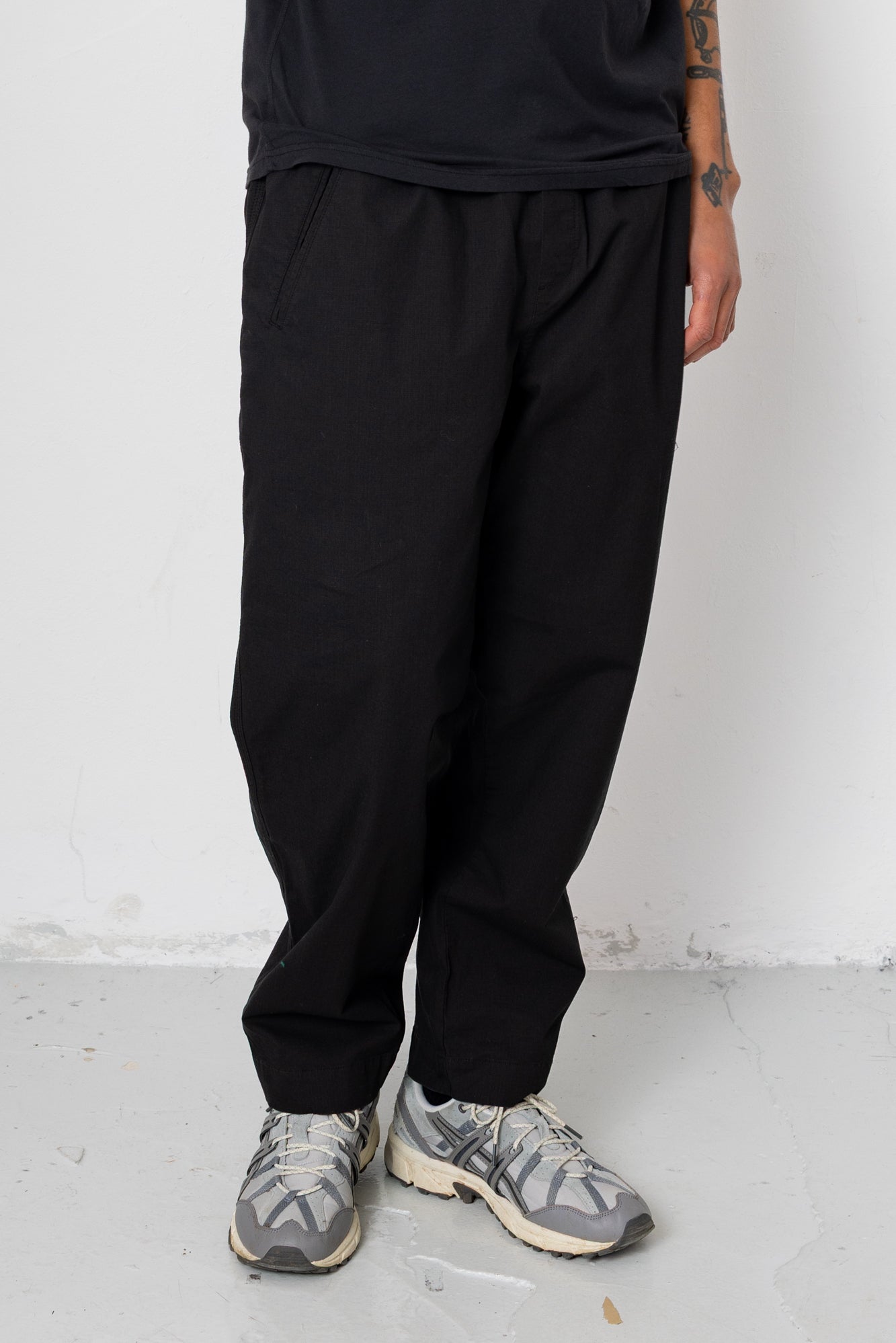 Person wearing black pants and gray sneakers against a white wall.