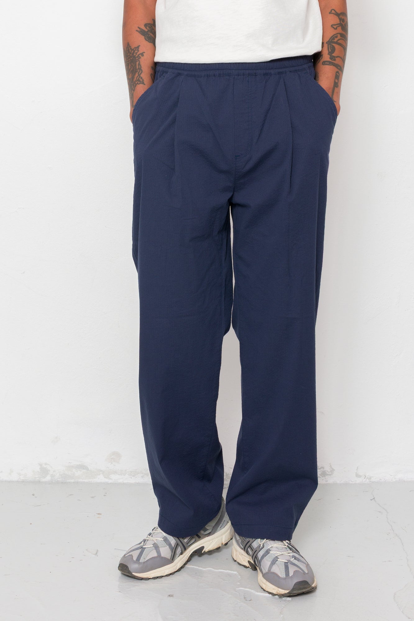 Person wearing navy pants and a white shirt against a white background