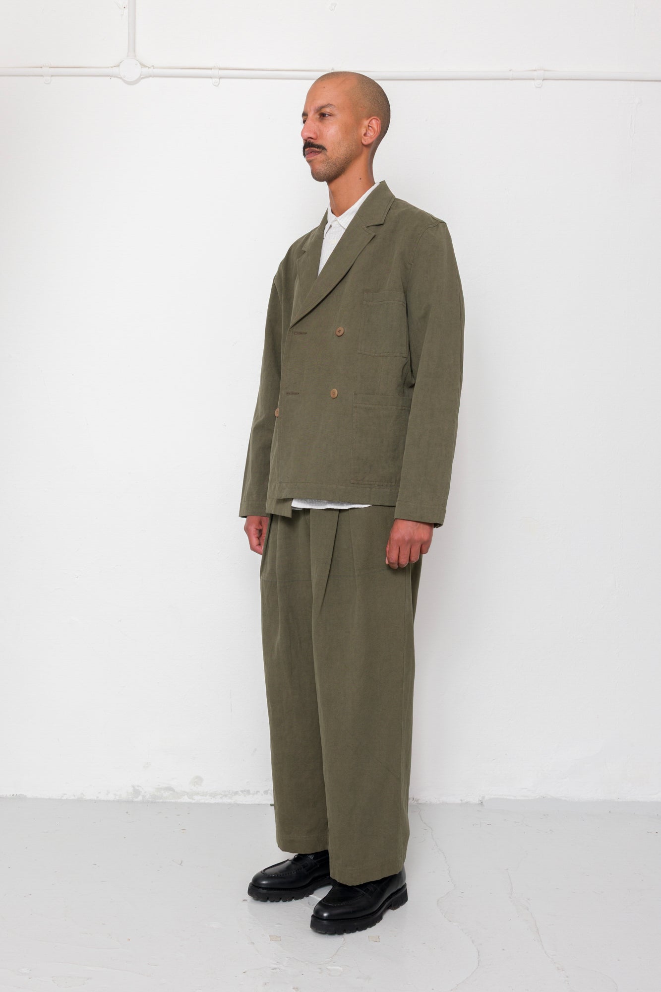 Man wearing a green suit standing against a white wall