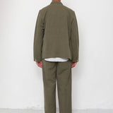 Person wearing a green jacket and pants standing against a white wall.