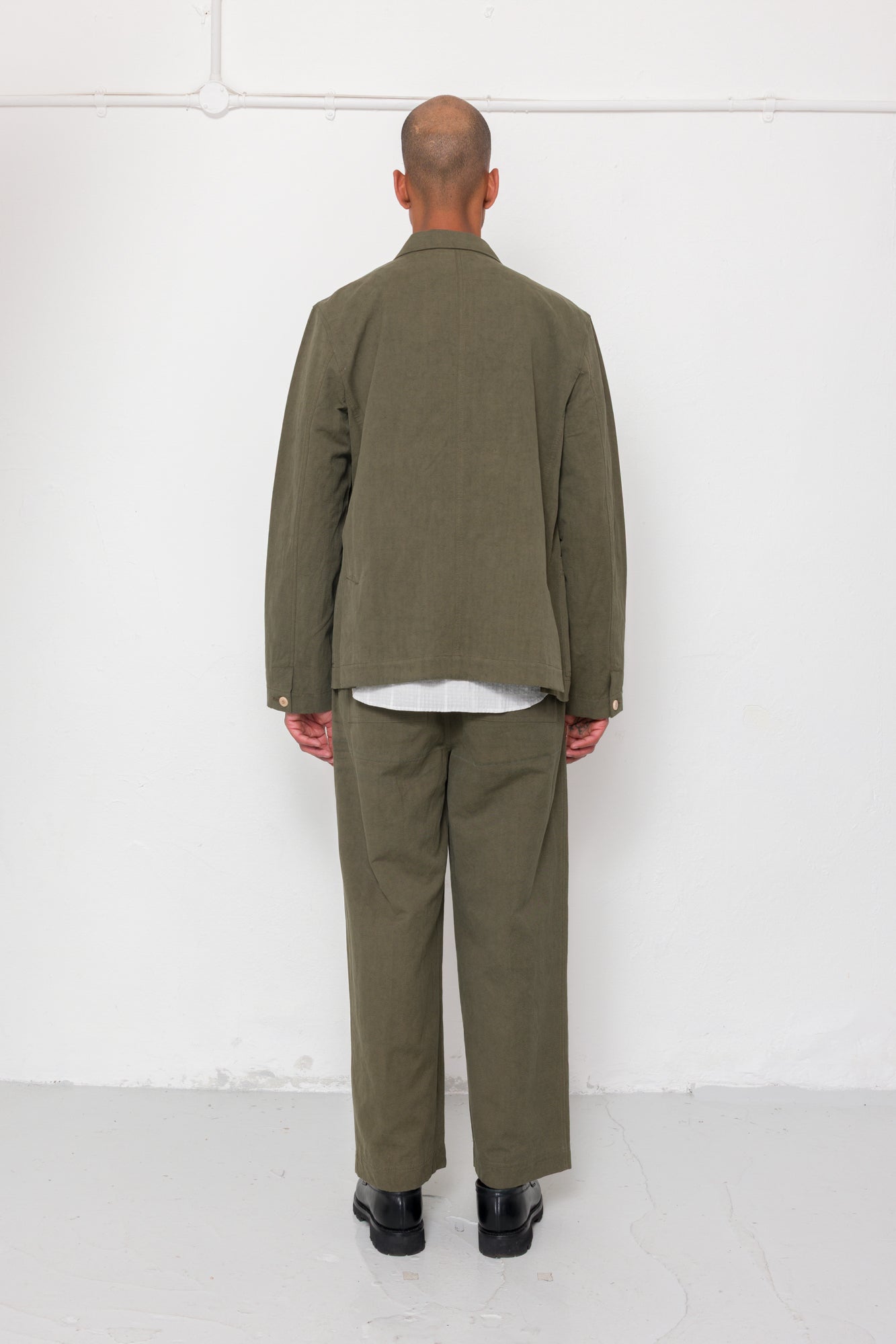 Person wearing a green jacket and pants standing against a white wall.