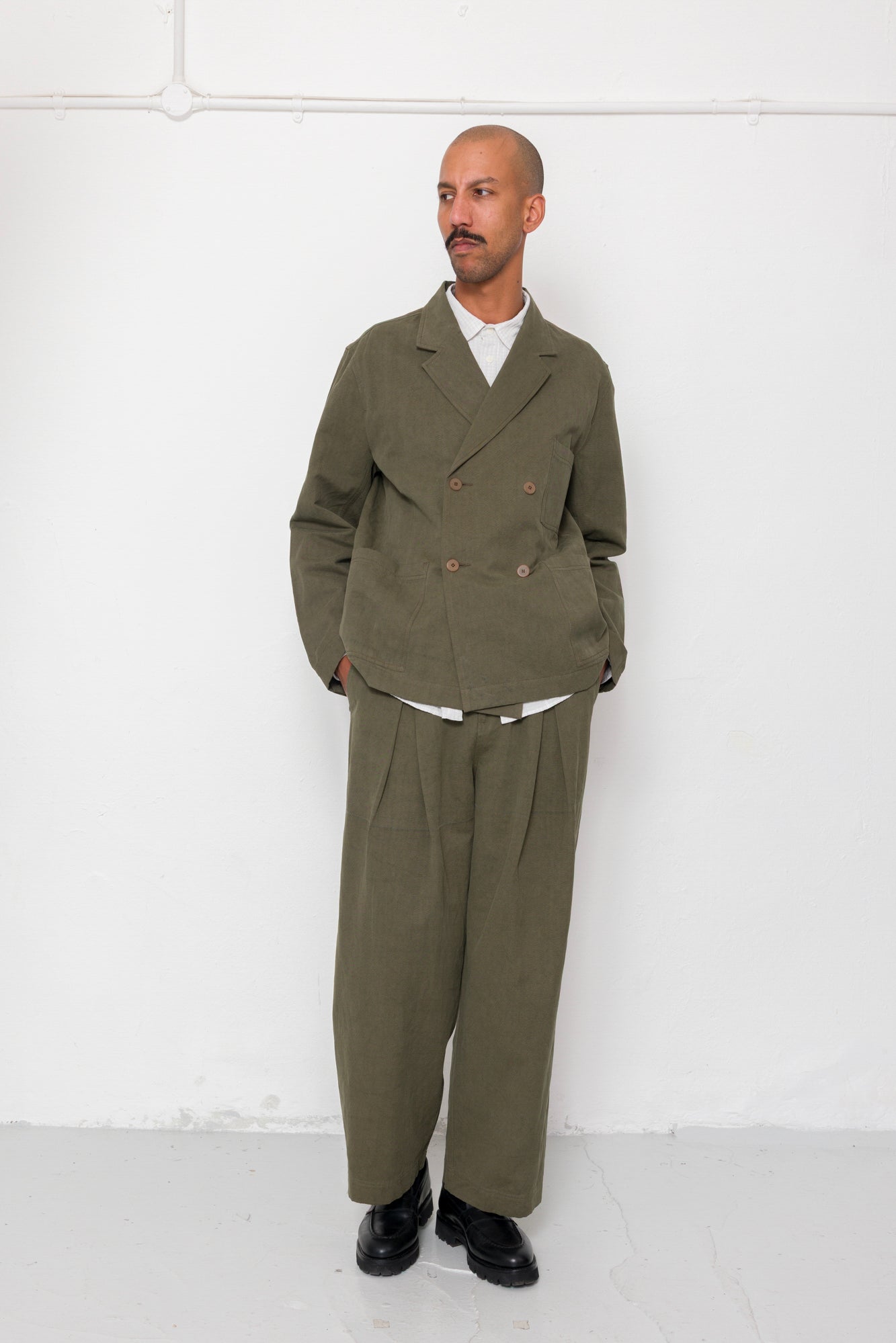 Man wearing a green suit standing against a white wall
