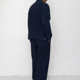 Man wearing a navy suit standing against a white wall