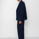 Man wearing a navy suit standing against a white wall