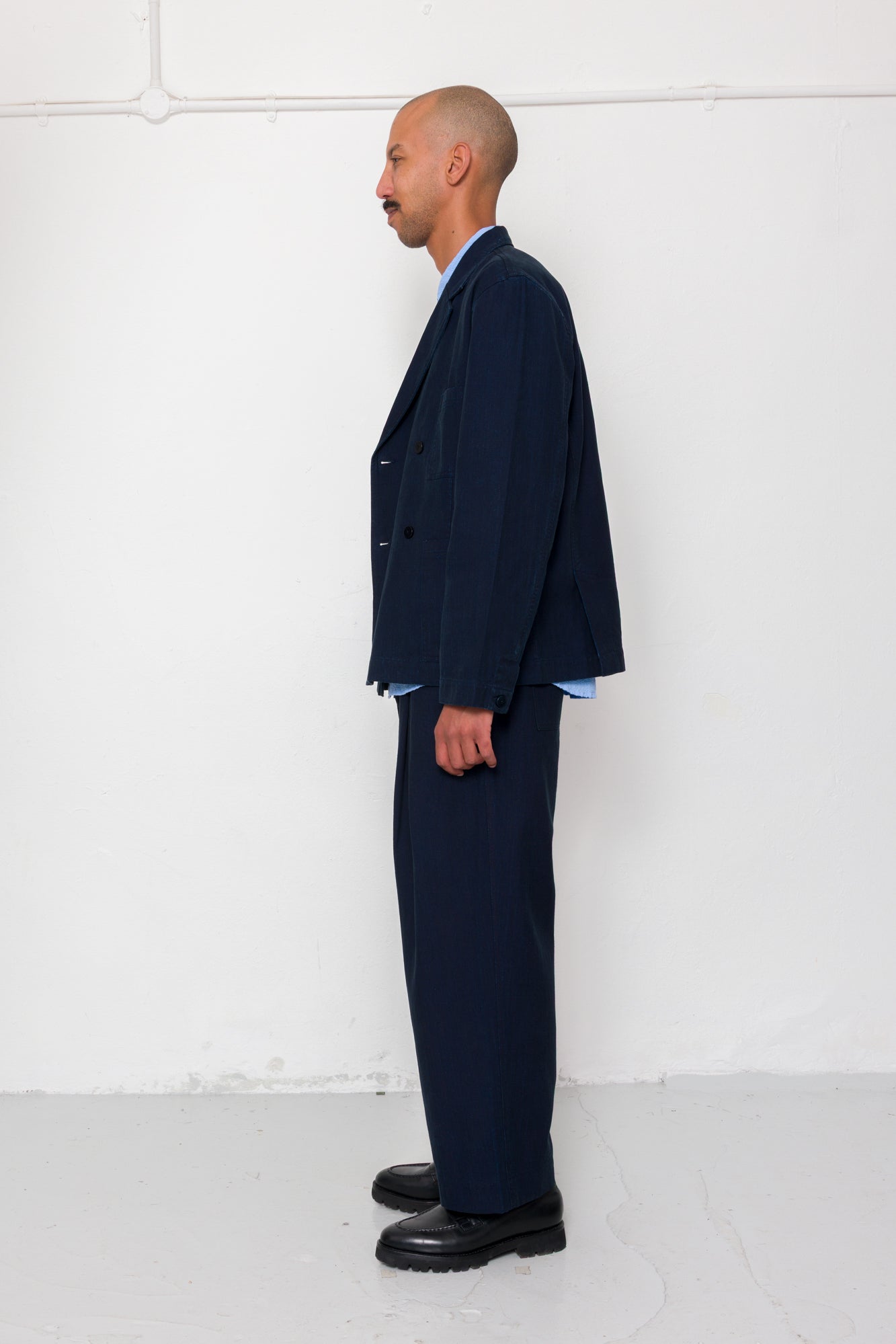Man wearing a navy suit standing against a white wall