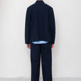 Person wearing a navy blue outfit standing against a white wall.