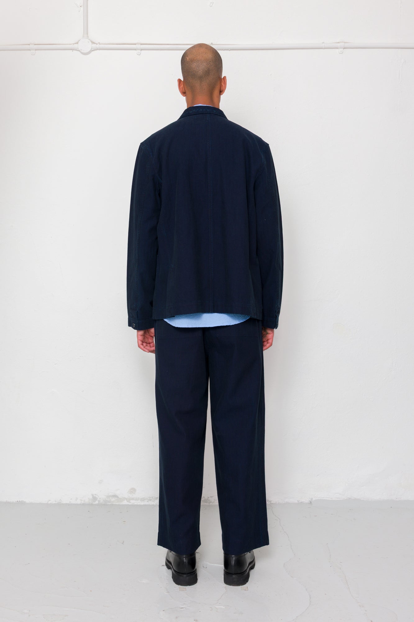 Person wearing a navy blue outfit standing against a white wall.