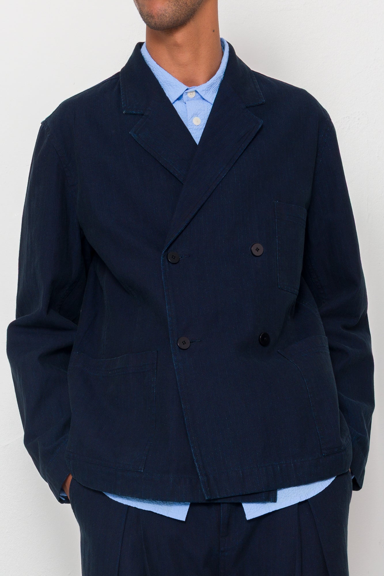 Man wearing a navy blue jacket over a light blue shirt on a white background