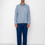 Man wearing a blue checkered shirt and dark pants against a white background