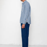 Man wearing a blue and white striped shirt and dark jeans standing against a white wall.