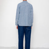 Person wearing a blue striped shirt and dark jeans standing against a white wall.