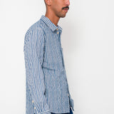 Man wearing a blue striped shirt and dark pants against a white background