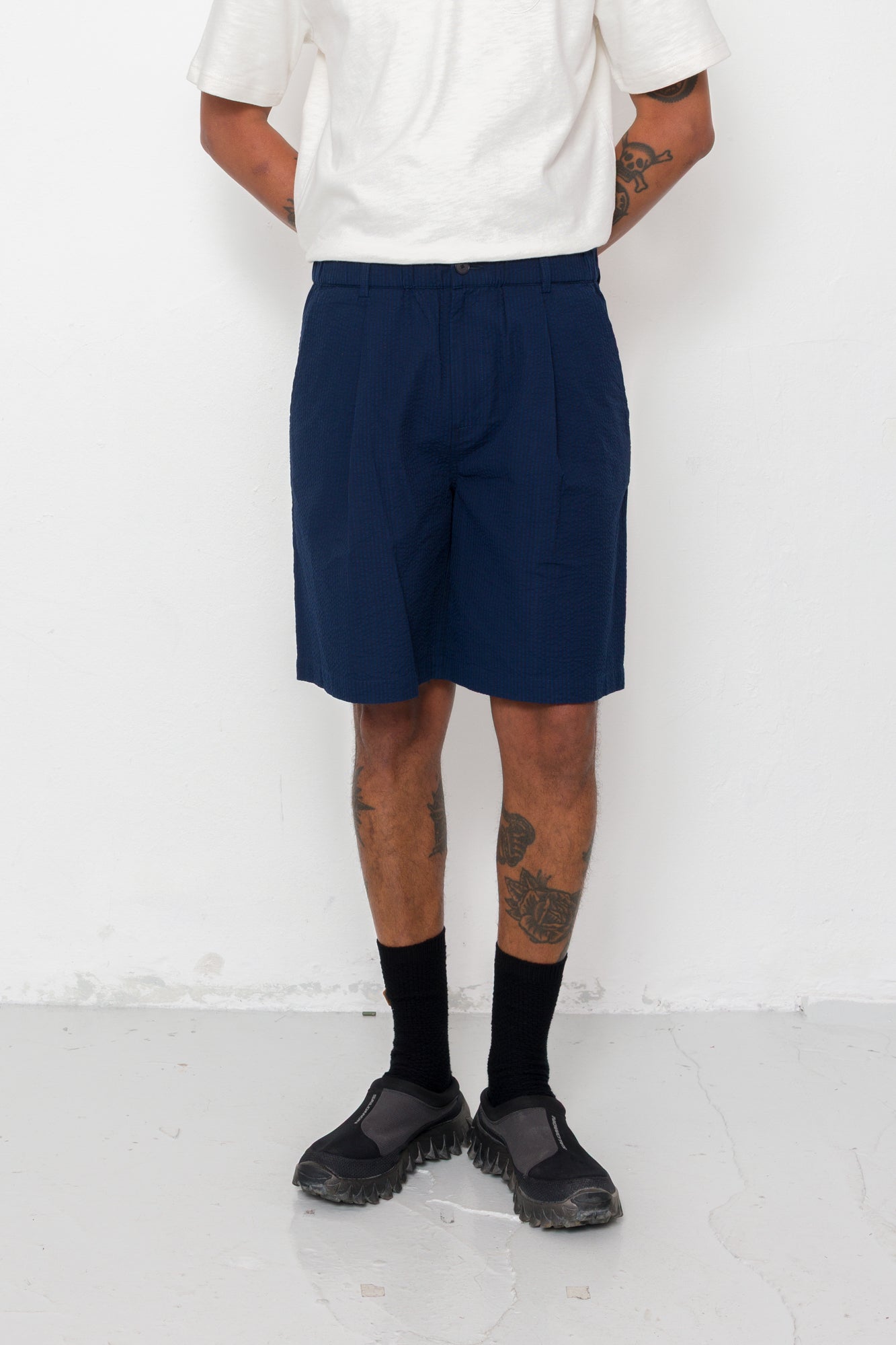 Person wearing navy shorts, white shirt, black shoes, and socks on a white background