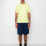 Man wearing a light yellow t-shirt and navy shorts against a white background