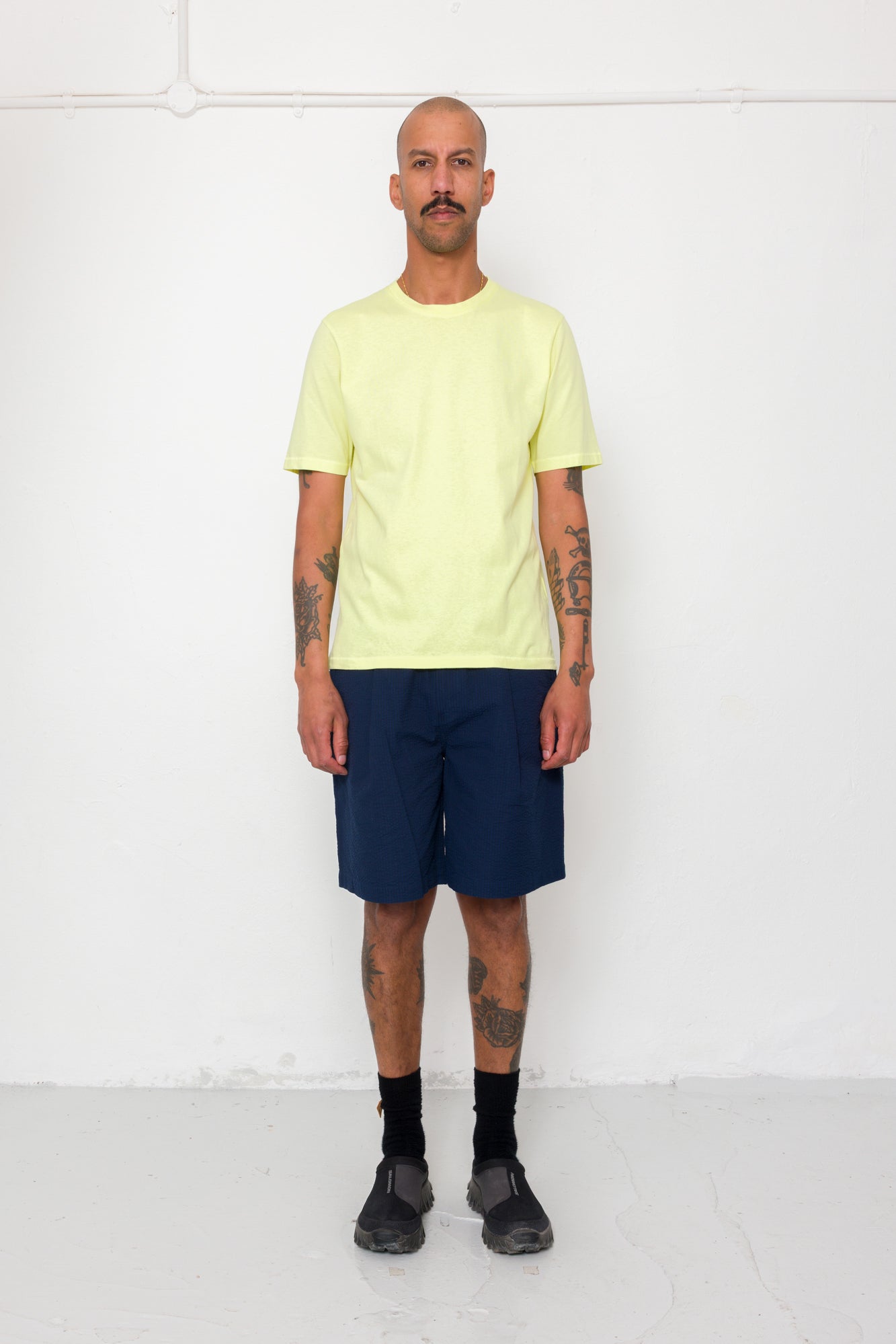 Man wearing a light yellow t-shirt and navy shorts against a white background