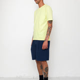 Man wearing a light yellow t-shirt, navy shorts, and black boots against a white background