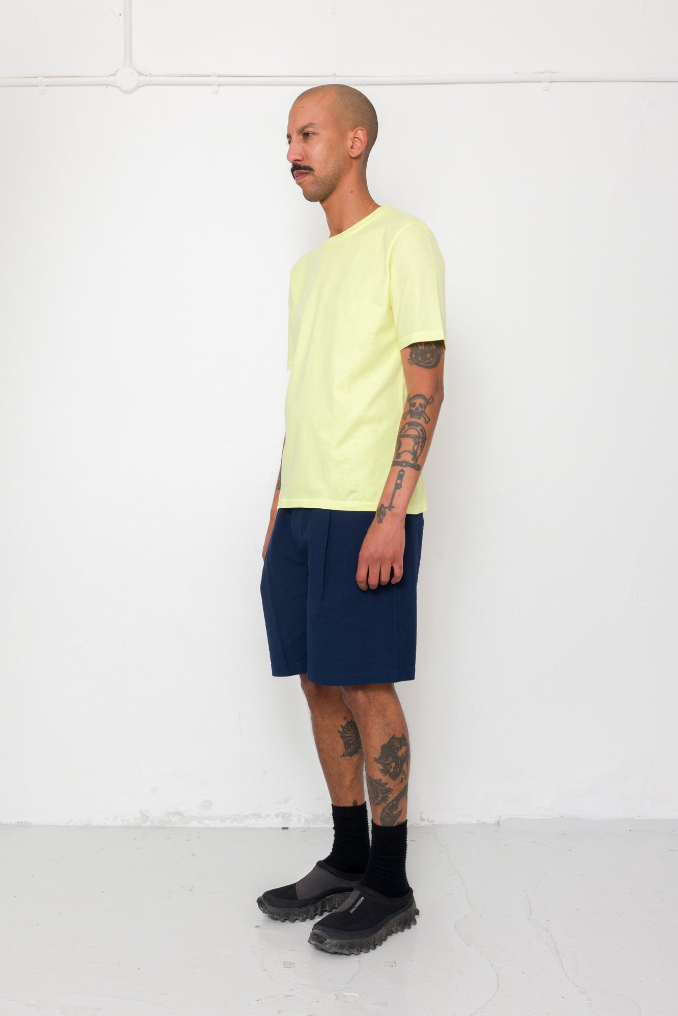 Man wearing a light yellow t-shirt, navy shorts, and black boots against a white background